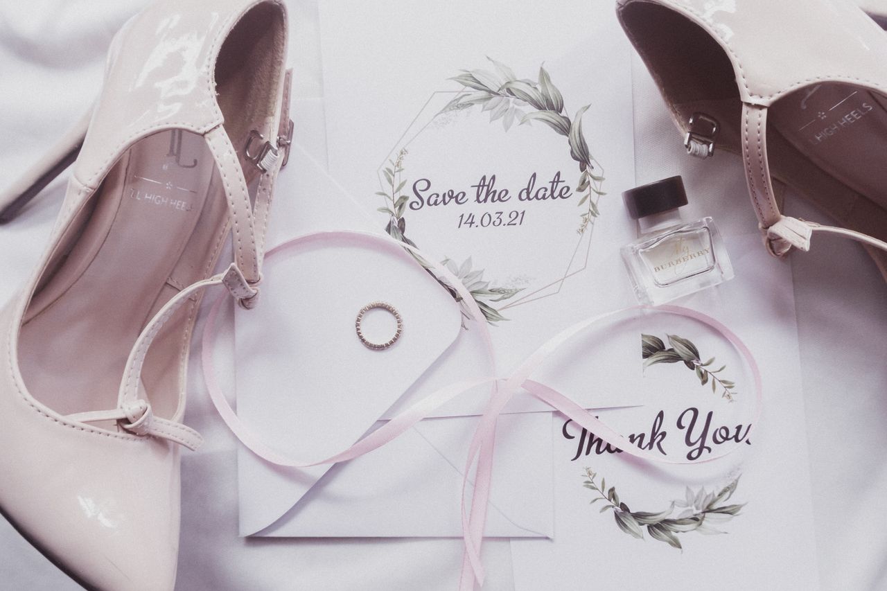why-choose-us Une élégante composition à plat d’éléments essentiels de mariage, avec des talons, du parfum et des invitations.
